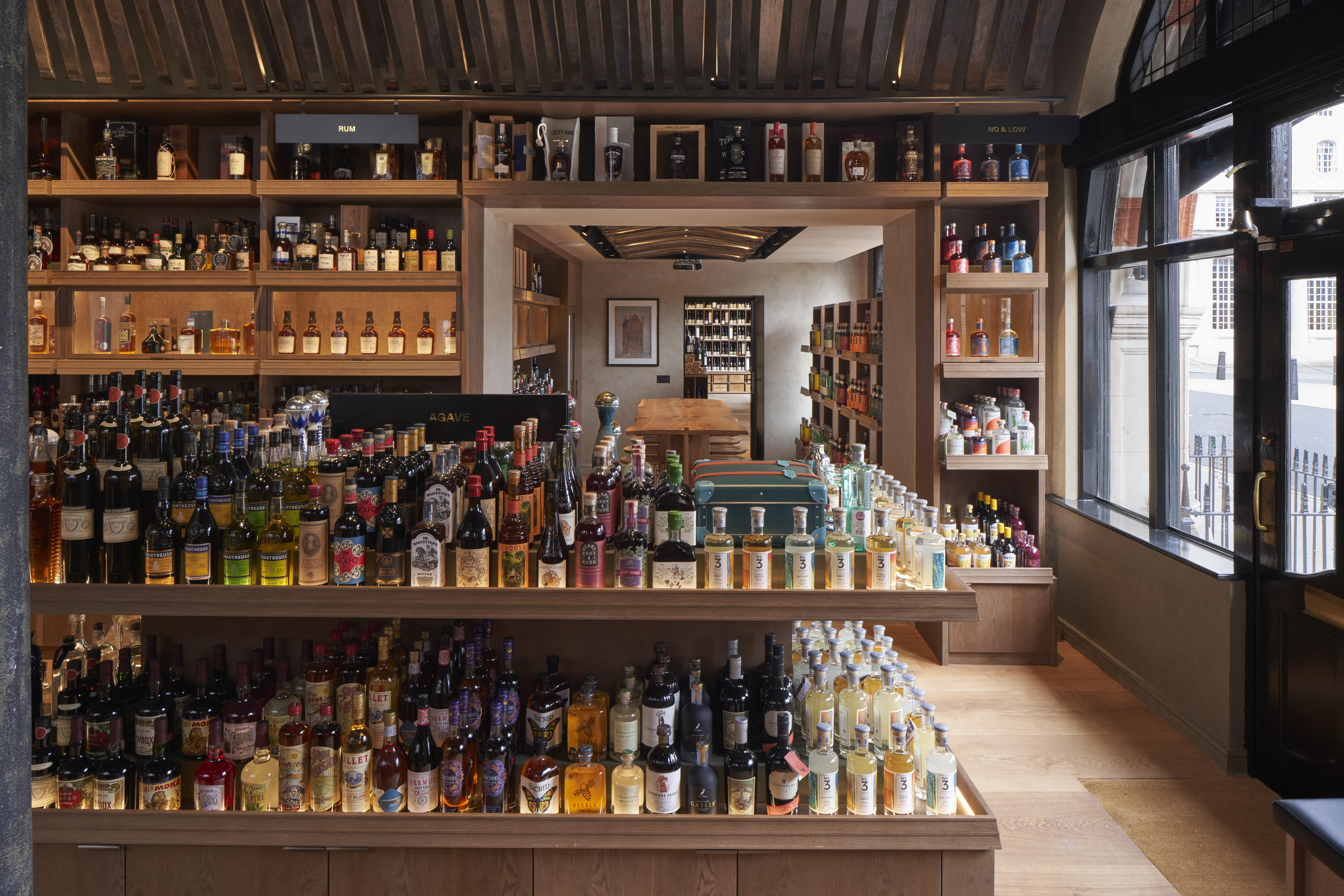 The interior of the Berry Bros. & Rudd spirits shop at No.1 St James’s Street, London, has a central display of premium spirits and agave bottles, with warmly lit shelving and natural light from the shopfront windows.