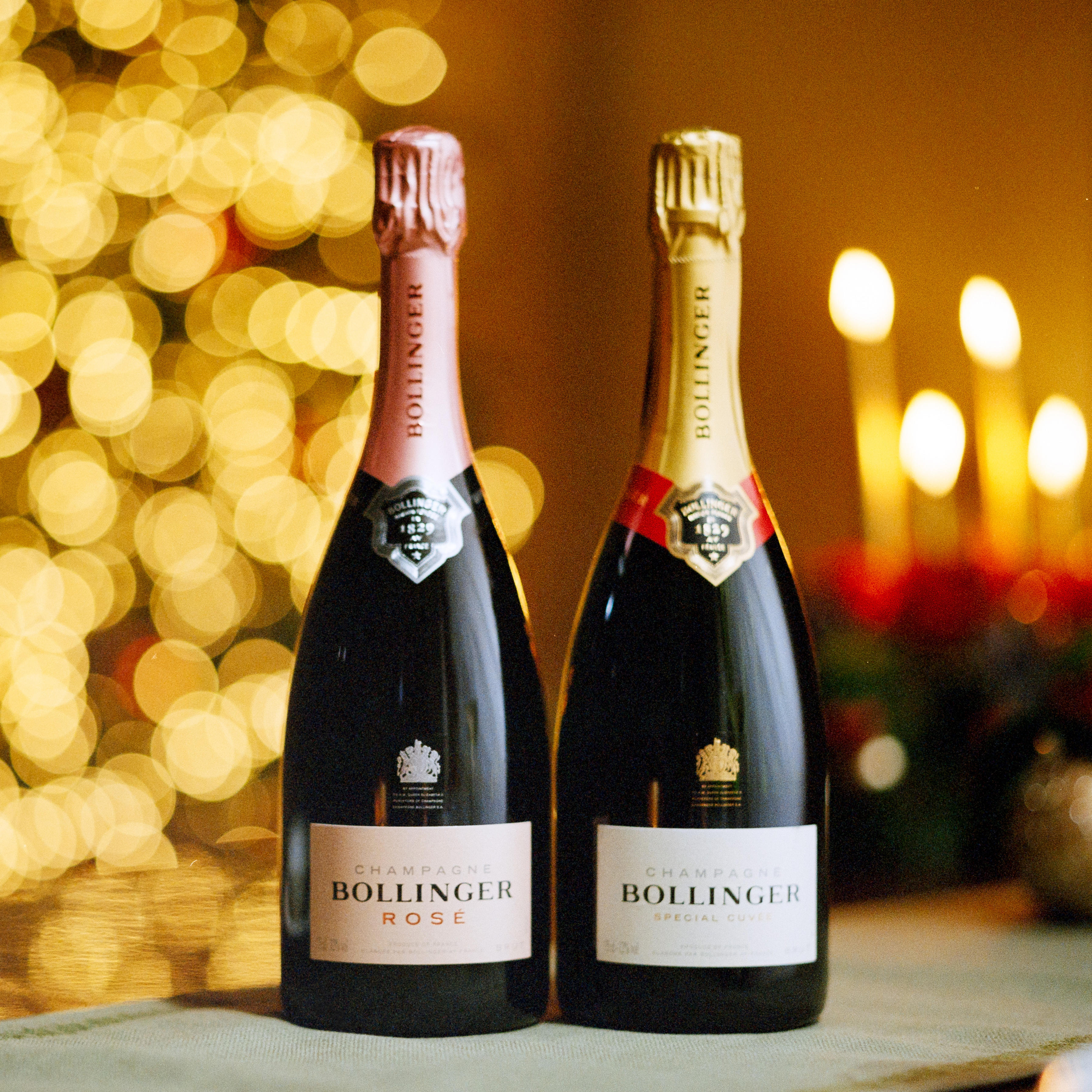 Two bottles of Bollinger Champagne, Rosé and Special Cuvée, on a festive table with warm candlelight and golden bokeh lights in the background. Save 25% at Berry Bros & Rudd.