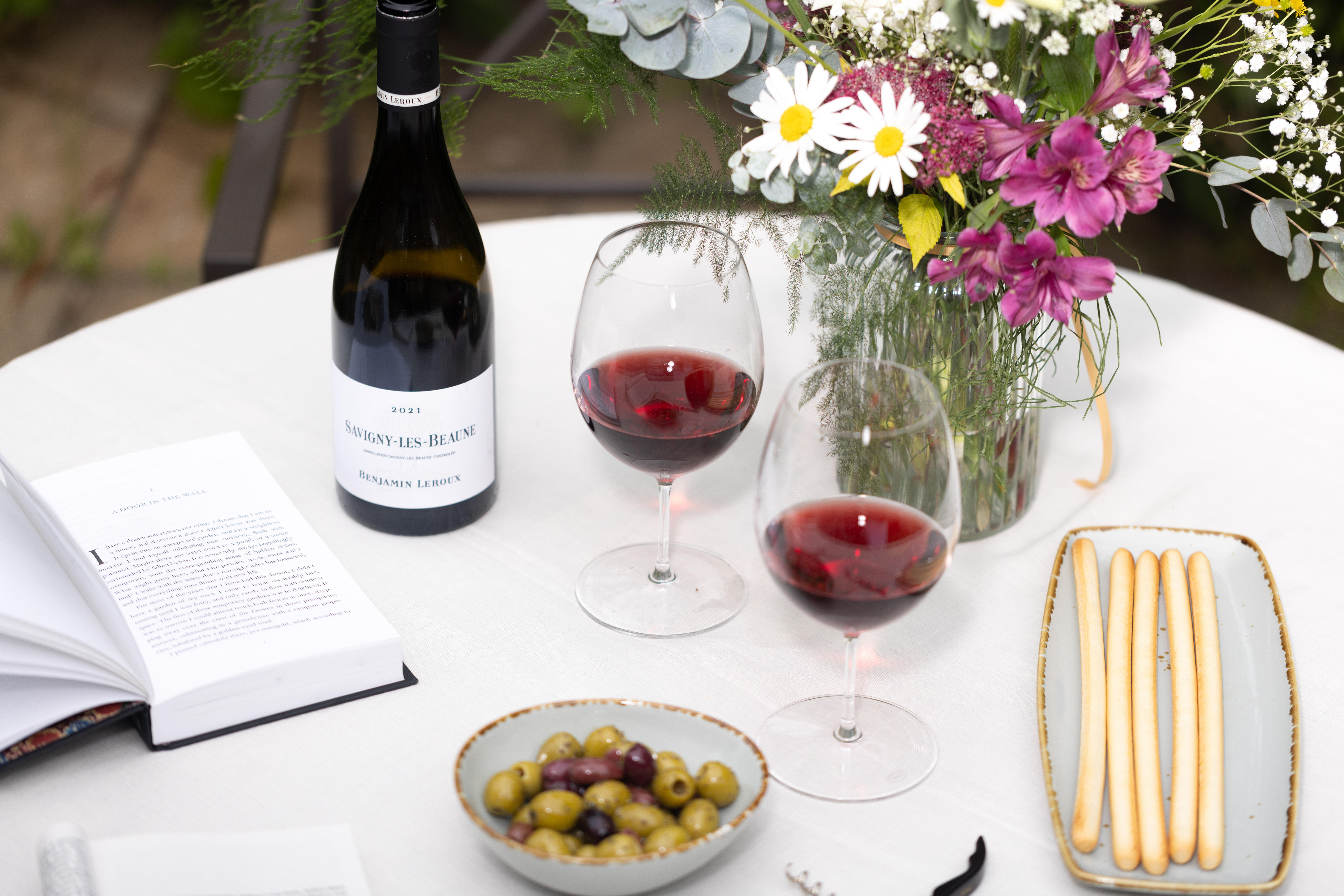 Glasses of red wine sitting on a table, surrounded by summer flowers